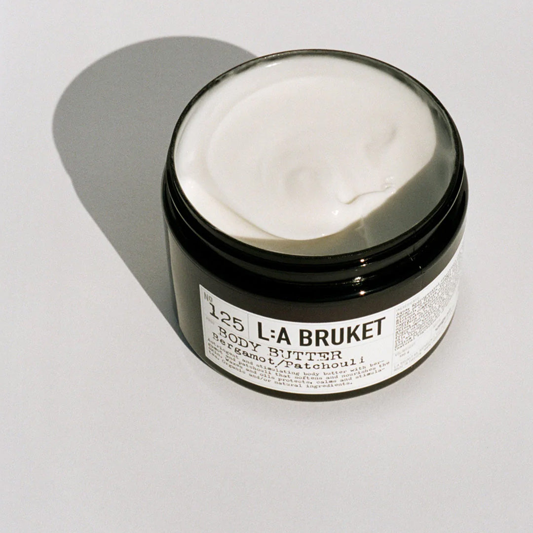 Bergamot and Patchouli Body Butter Detail 125 from L:A Bruket on table with open lid. Bergamot and Patchouli gives a warm fresh herbal and spicy scent. A soothing, nourishing body cream from L:A Bruket providing moisture to dry and dehydrated skin and stimulating cell renewal. Contains cocoa butter, babassu seed oil and beeswax as well as essential oil from bergamot and patchouli.
